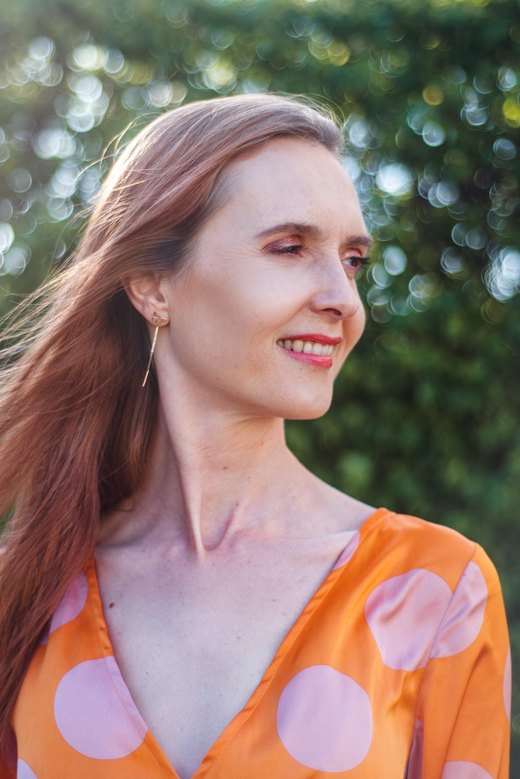 Barbara Jońca w ogrodzie, w pomarańczowej sukience, w świetle zachodzącego słońca